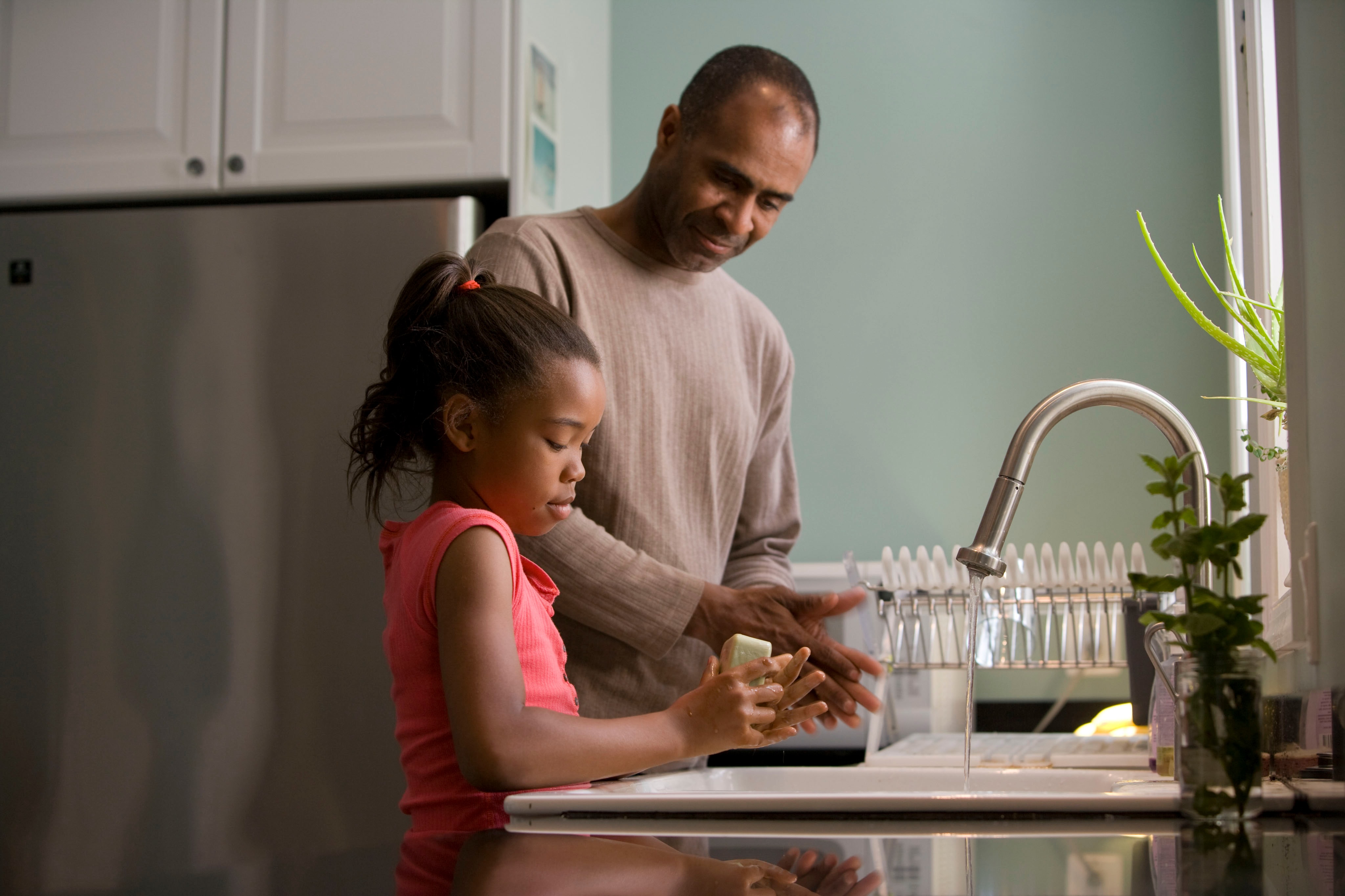 father and daughter standing over a kitchen sink washing their hands with a bar of soap